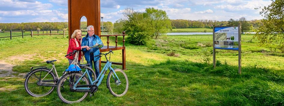 Man and woman stands by one of the ten artworks you can find when cycling the Meuse Cycle Route Limburg