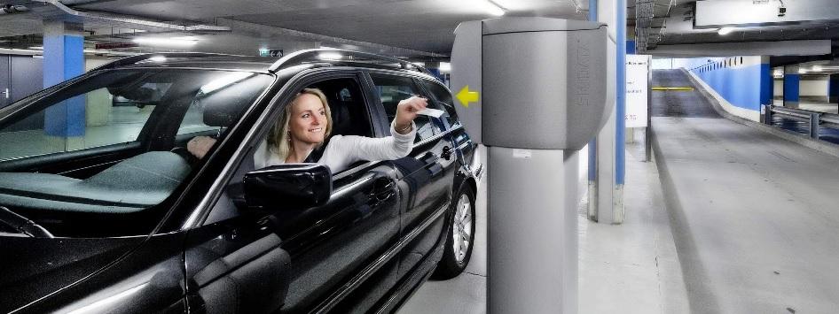 Vrouw in een auto die een parkeerkaartje pakt bij de ingang van een overdekte parkeergarage tijdens het parkeren in Roermond