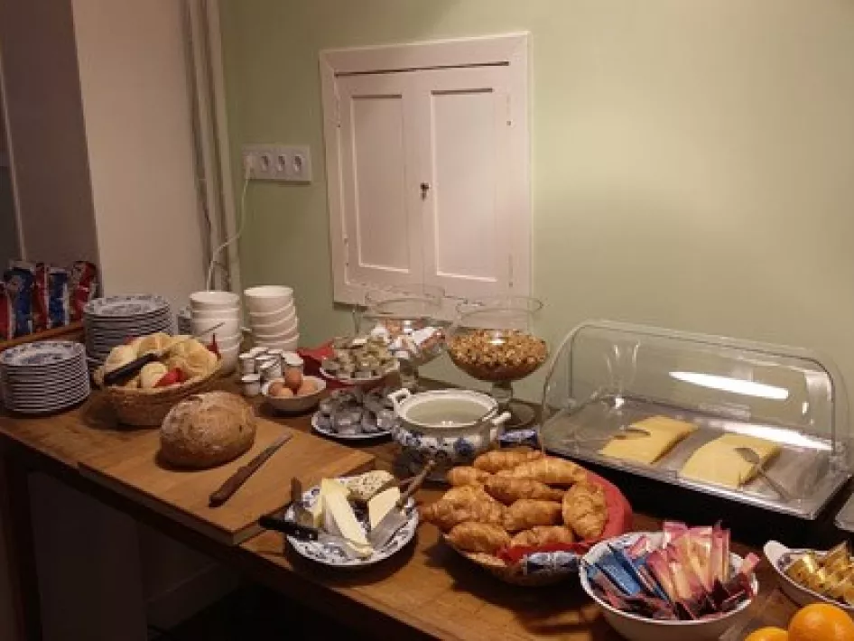 A full buffet breakfast at B&B Willem II, with freshly baked bread, croissants, cheese, cereal, fruit, eggs and various toppings options, presented on a wooden table in an attractive room with a soft green wall.