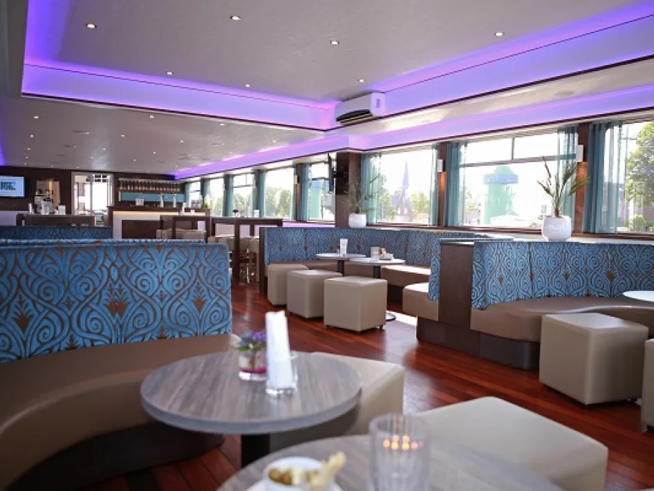 Luxe lounge op een schip met moderne zitbanken, paarse LED-verlichting en een stijlvolle bar.