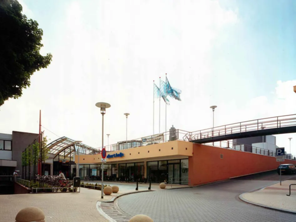 Muntpassage parking deck in Weert with entrance, ramp and bicycle parking, seen from the square with flags on the roof.