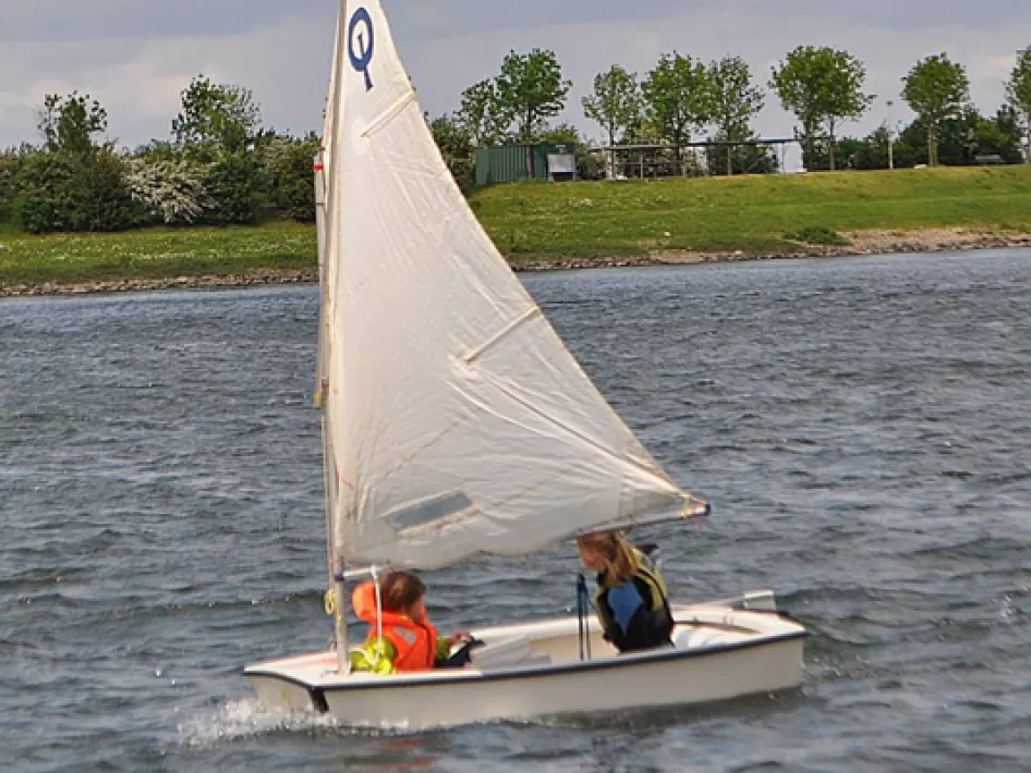 Zwei Kinder in einem kleinen Segelboot auf der Maas beim Segeln während einer Wassersportaktivität in der Nähe des Hafens von Neer.