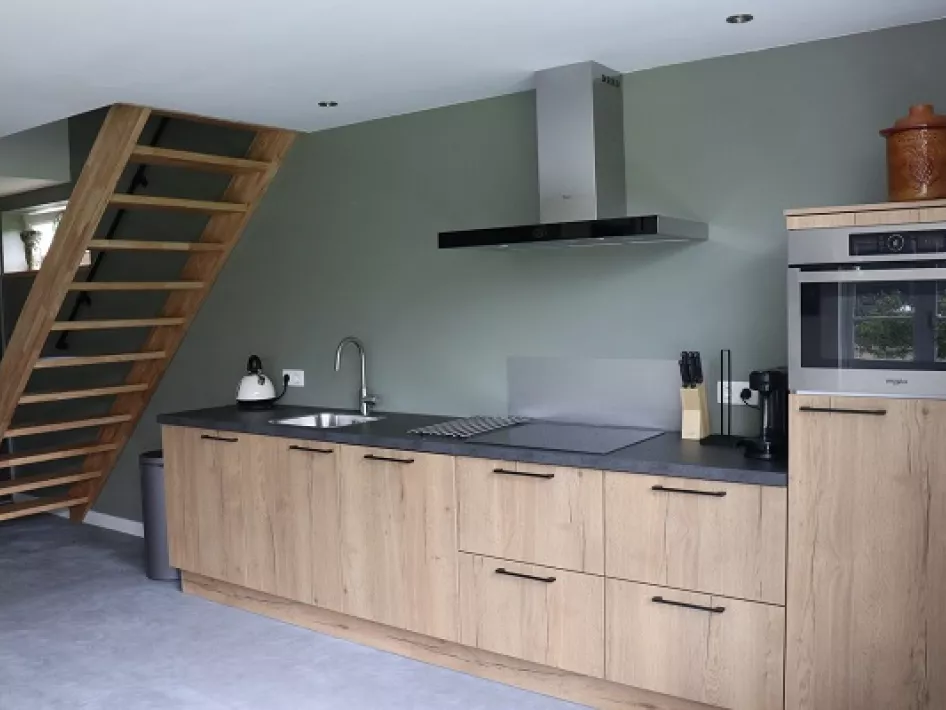 Moderne open keuken met houten kastjes, een trap naar de vide en een strakke, minimalistische inrichting.