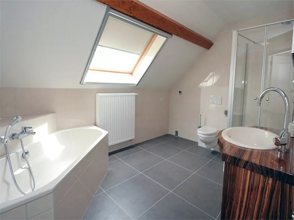 Moderne badkamer met ligbad, douche, toilet en wastafel onder een dakraam