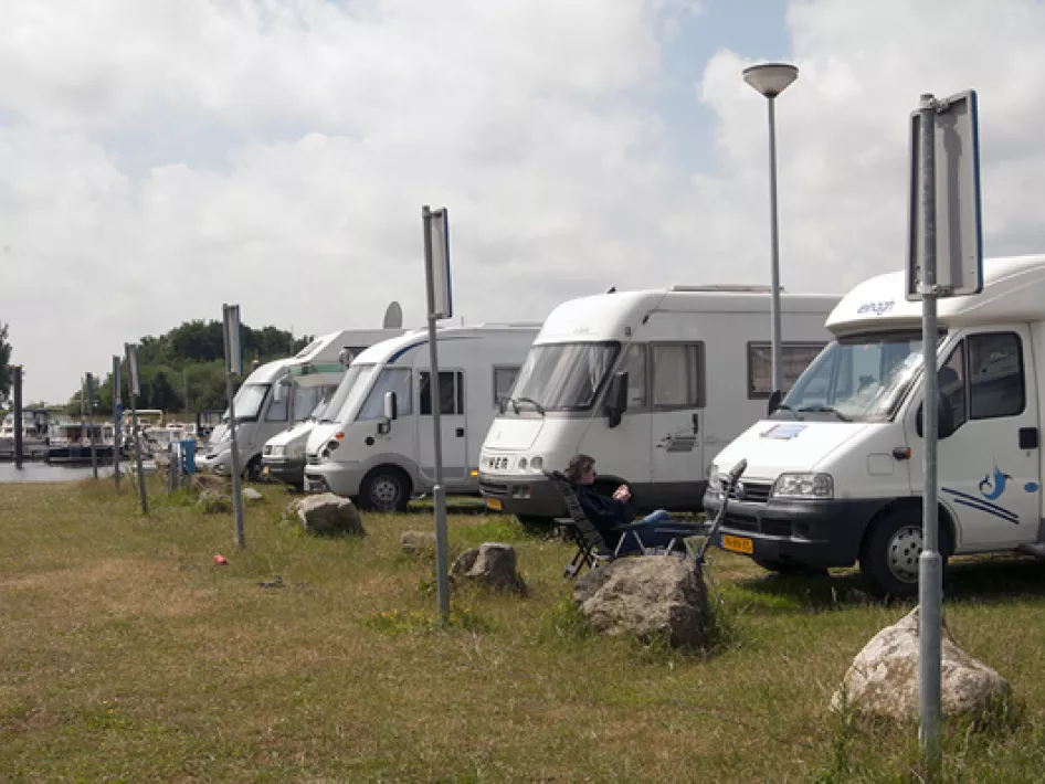 Reihe von Wohnmobilen auf dem Wohnmobilstellplatz an der Maas in Neer, mit Blick auf das Wasser und Platz zum Sitzen im Freien.