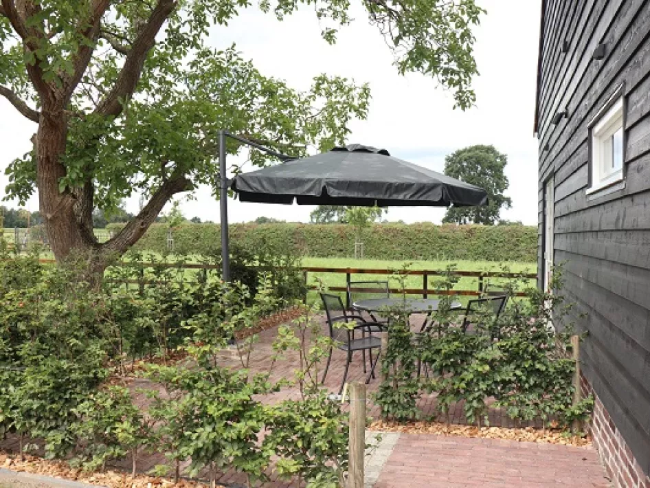 Gezellig terras met zitgelegenheid en parasol, omringd door groen en gelegen naast een zwarte houten gevel.