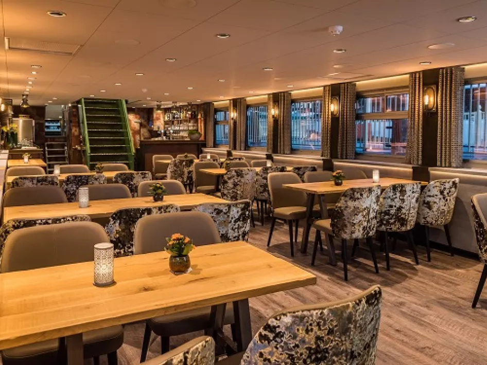 Sfeervolle eetruimte op een schip met houten tafels, comfortabele stoelen en warme verlichting.