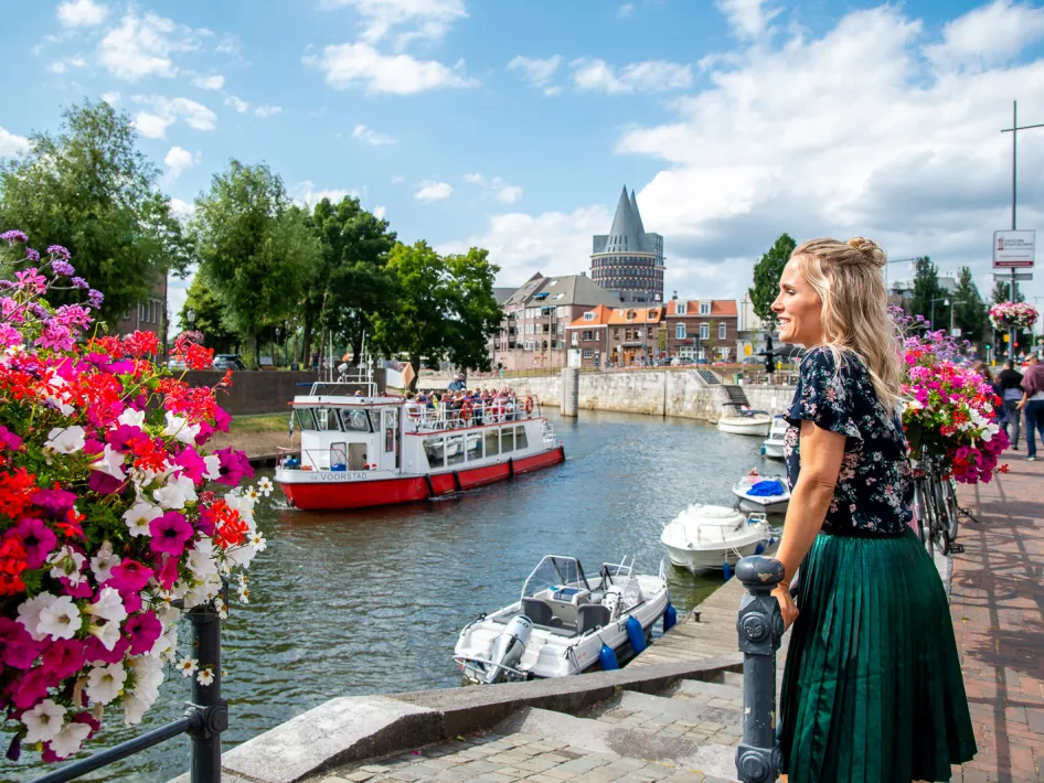 Vrouw kijkt over de balustrade van de Roerkade waar op de achtergrond de rondvaartboot van Rederij de Corporaal aanmeert