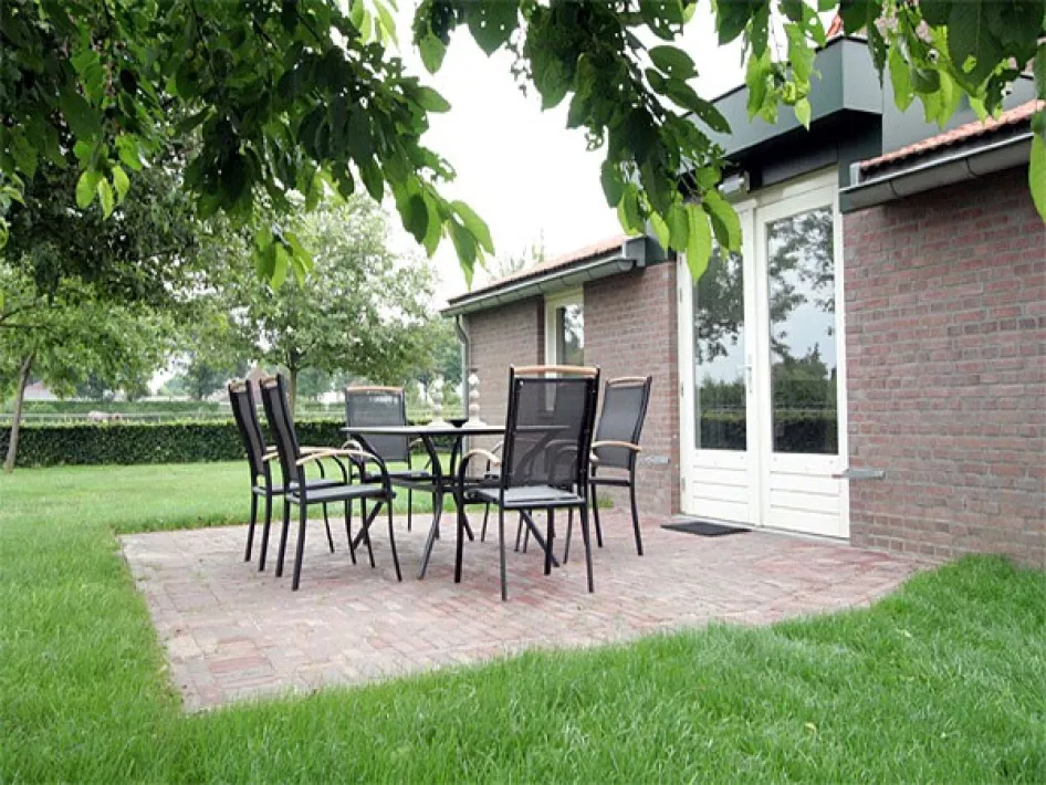 Terras met tuinstoelen en tafel naast het vakantiehuis in een groene omgeving