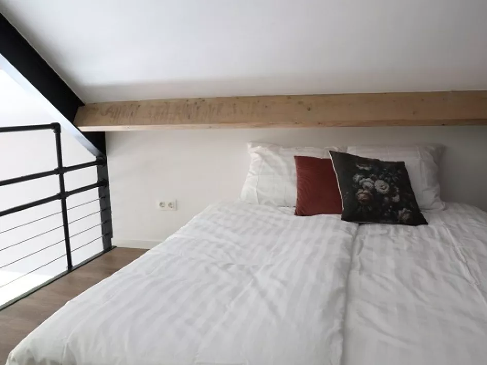 Knusse slaapvide met een tweepersoonsbed onder een houten balk en uitzicht op de benedenverdieping.