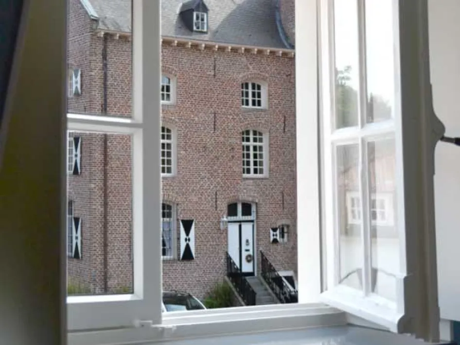 View through an open window of a characteristic brick castle with white shutters.