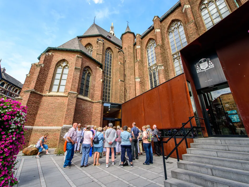 Groep mensen bij de ingang van het Historiehuis in Roermond, met op de achtergrond de oude gevel van de Munsterkerk.