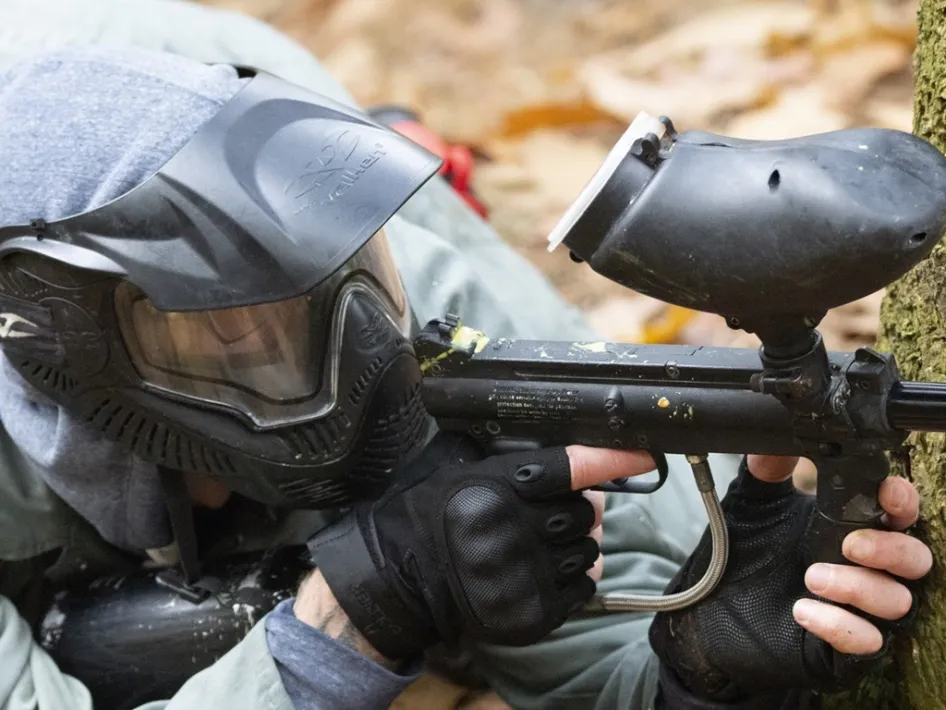 Een paintballspeler van 360Adventures richt zijn geweer vanuit een schuilpositie in een bosrijke omgeving.