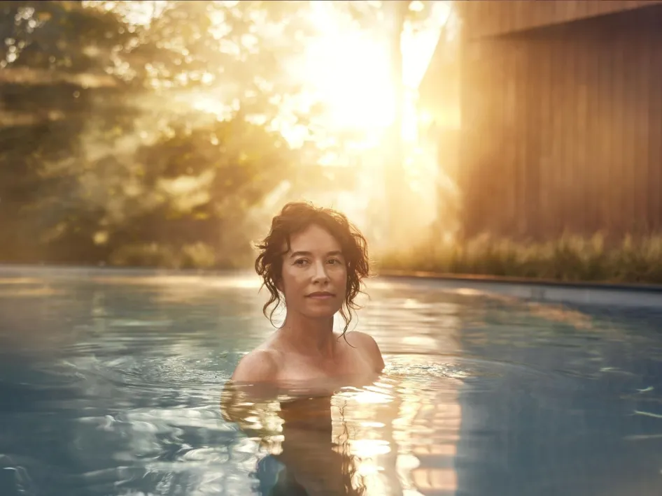 Vrouw in het buitenbad. Achter haar is een laaghangende zon te zien