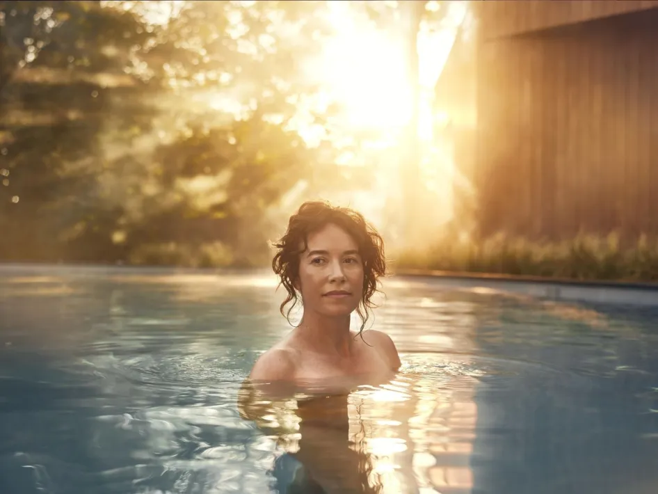 Vrouw in het buitenbad. Achter haar is een laaghangende zon te zien