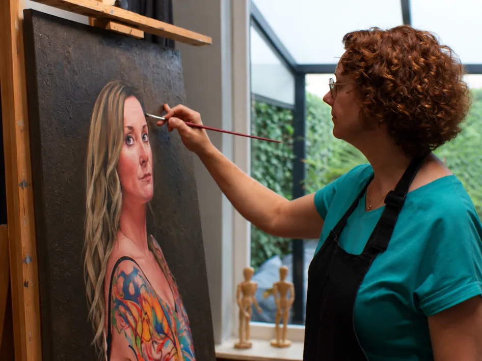 Kunstenares schildert een portret van een vrouw tijdens het maken van een realistisch schilderij, passend bij de expositie Kunstkring Artimosa in Bibliotheek Reuver.