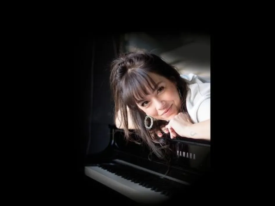 Portret van Linda Smeets leunend bij een piano, met een warme blik en een intieme sfeer in zacht licht.