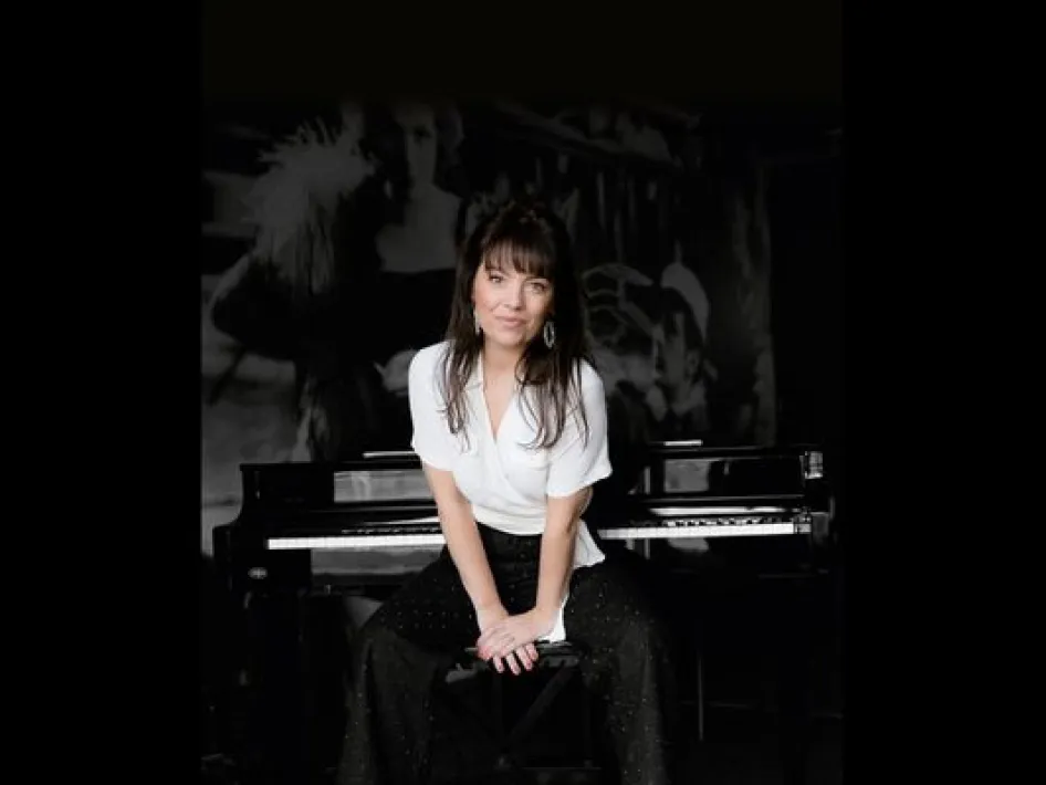 Portret van Linda Smeets zittend voor een piano, met een rustige blik en een intieme, donkere setting.