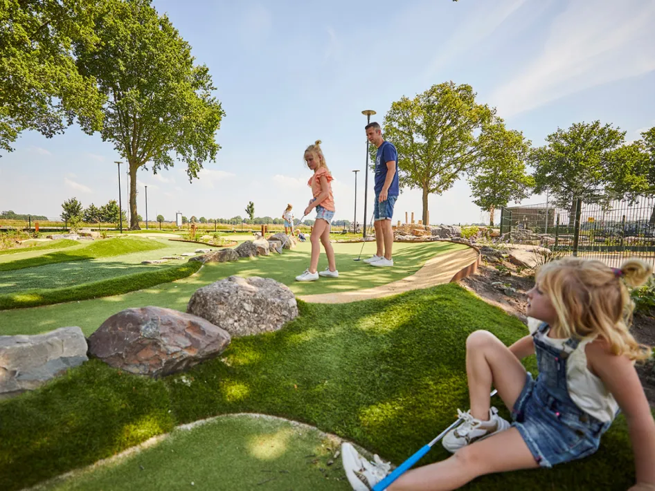Meisje maakt een swing terwijl haar zusje toekijkt, tussen de rotsen en heuveltjes op de golfbaan.