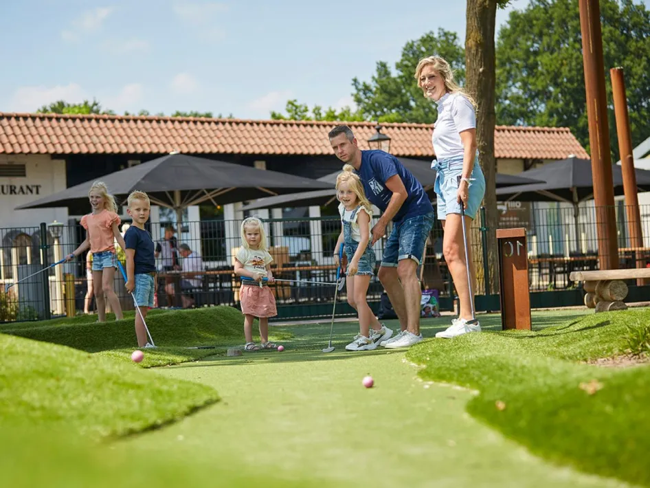 Gezin speelt minigolf voor het restaurant bij de Leistert, met uitzicht op het terras en het groen van de baan.