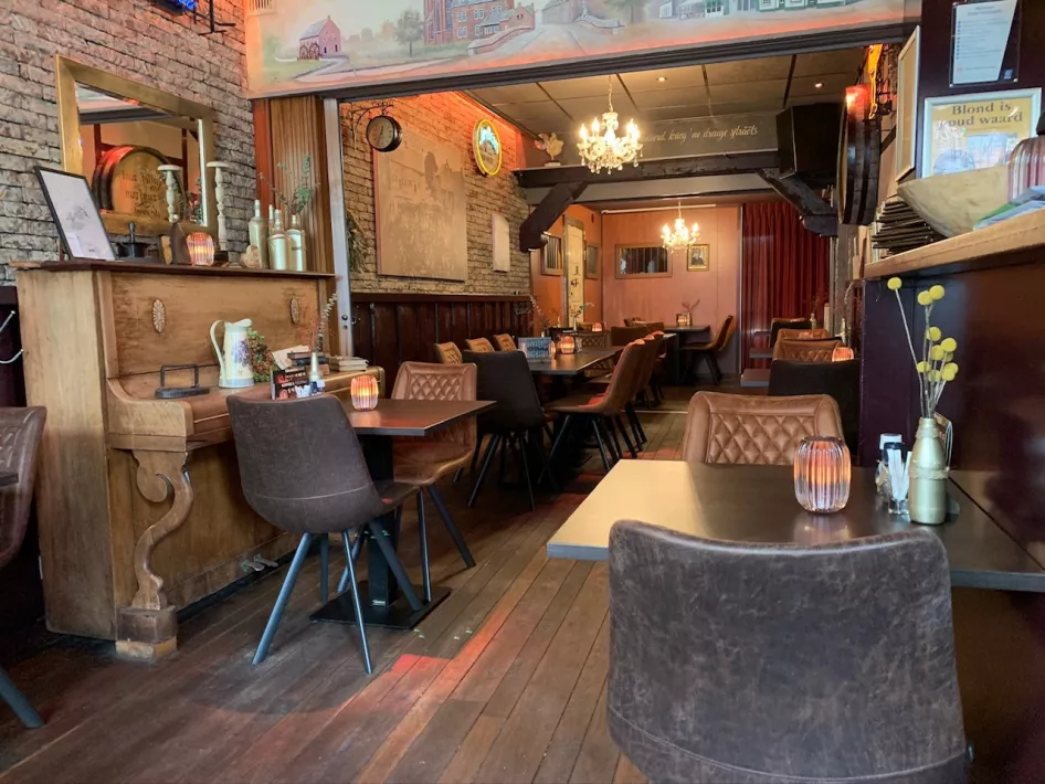 Cozy and attractively decorated eatery with wooden floor, brown leather chairs and warm lighting. The space has a classic look with decorative elements such as an old wooden dresser, candles on the table and a chandelier on the ceiling.