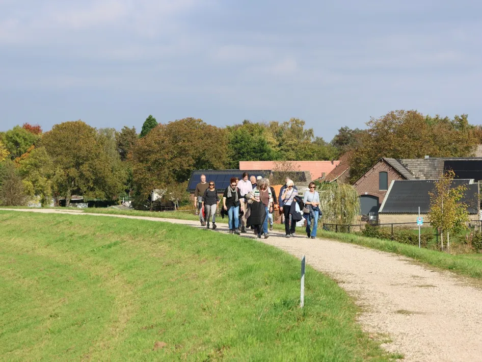 Groep wandelaars tijdens de Akoestische Wandeling Beesel op een landelijk pad langs grasvelden en boerderijen.