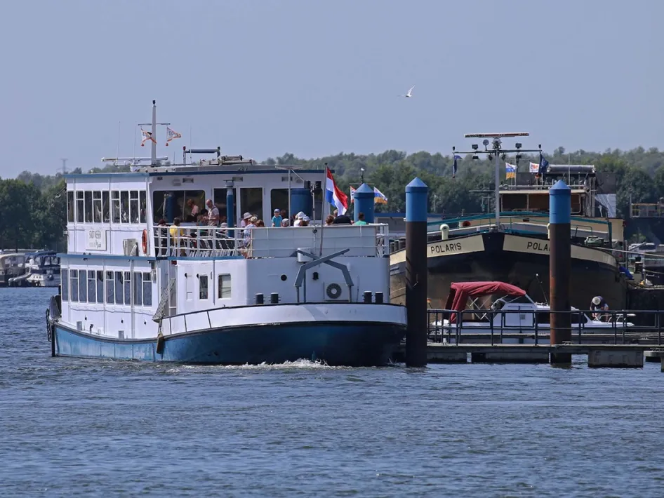 Luxe passagiersschip op de Maas, perfect voor een culinaire Asperge Cruise, met gasten aan boord en een Nederlandse vlag op de achtersteven.