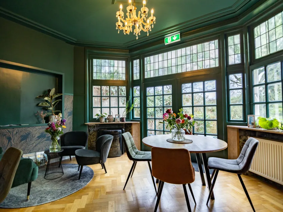 Inviting lounge at B&B Willem II with classic windows, a chandelier and a cosy seating area.
