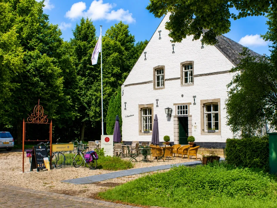 White historic building of ’t Kapelhuis in Thorn with a terrace and seating under the trees.
