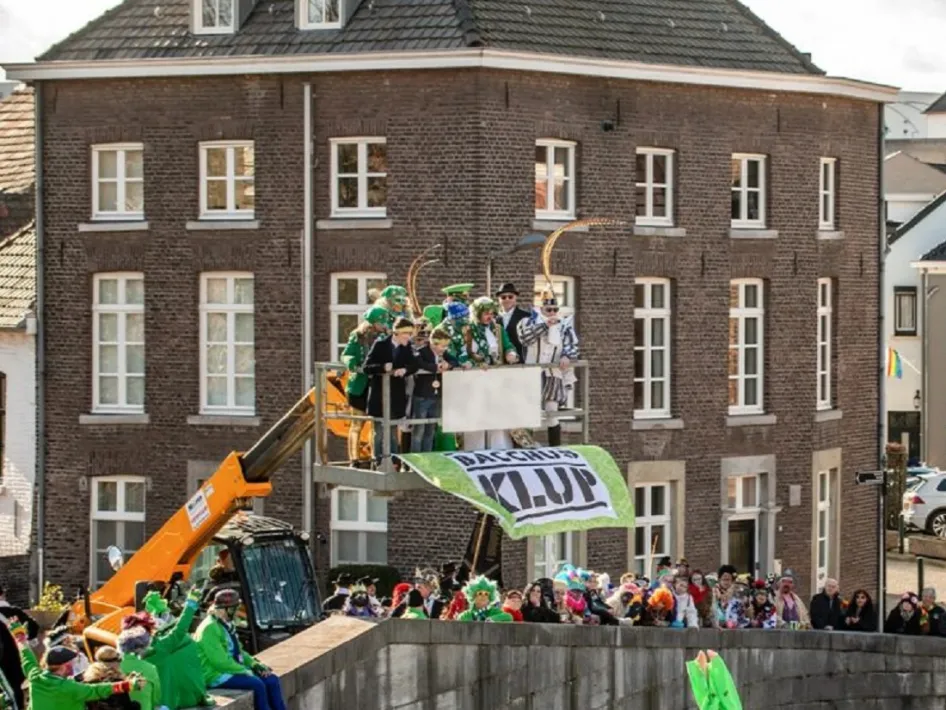Bacchusdrieve in actie – Carnavalsvierders worden tijdens het traditionele Bacchusdrieve met een hoogwerker over de Maas gehesen, terwijl toeschouwers het spektakel volgen.
