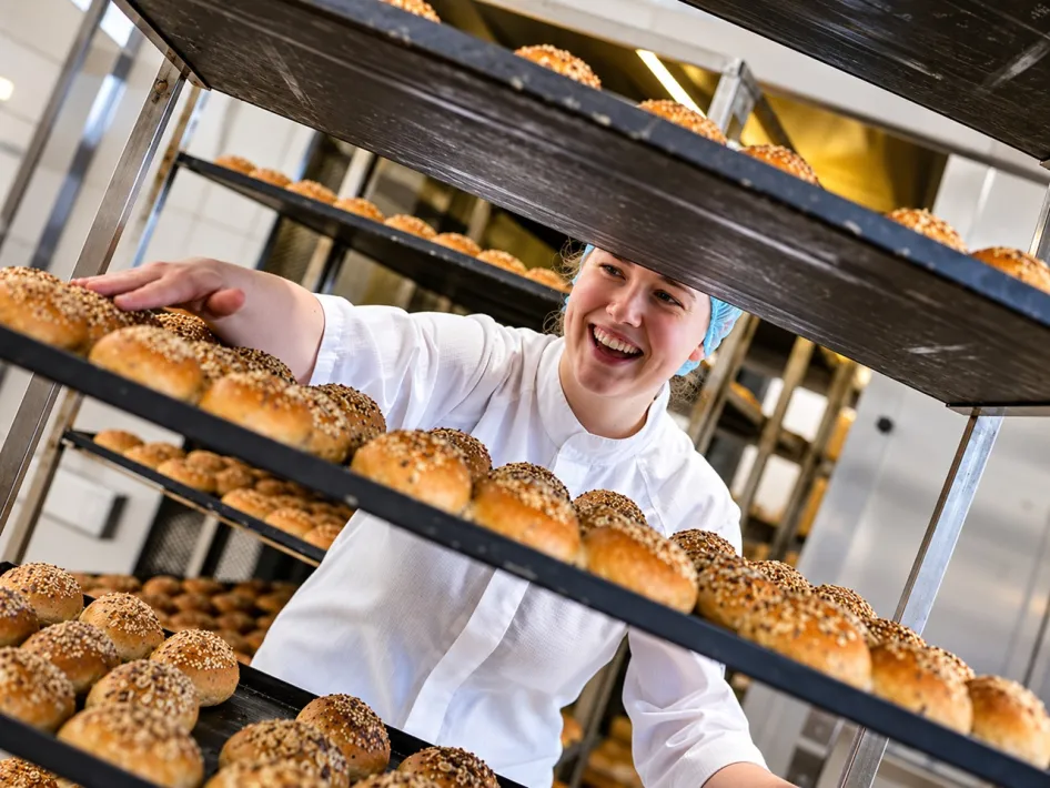 A baker places freshly baked bread rolls on a rack at Heerschap Bakery.
