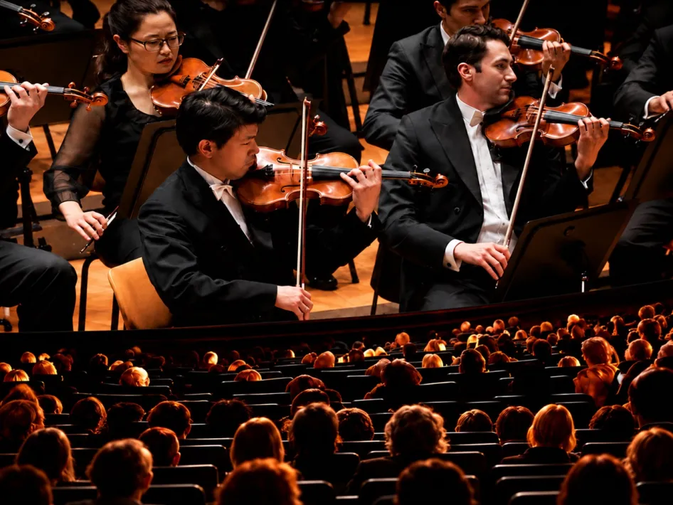 Bezoekers in een bioscoopzaal kijken op het witte doek naar Berlin Philharmonic: New Year's Eve Concert 2026, met violisten van het orkest in beeld.