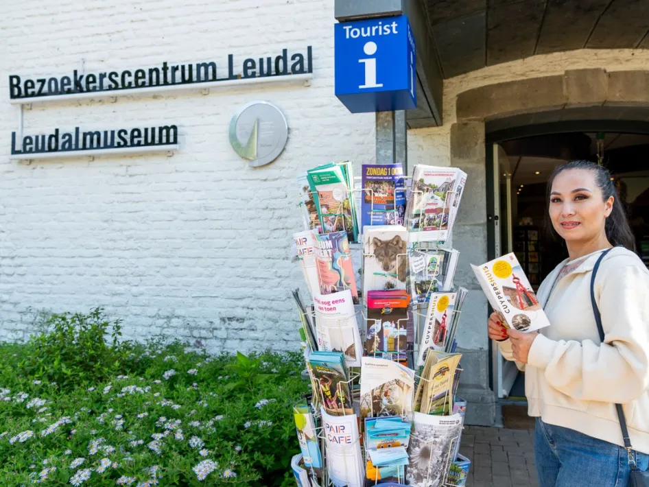 Vrouw pakt een folder uit een rek met toeristische brochures bij de ingang van Bezoekerscentrum Leudal en Leudalmuseum