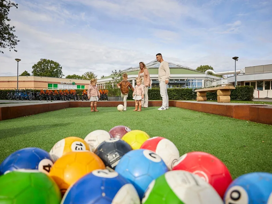Gezin speelt biljartvoetbal bij de Leistert met grote gekleurde ballen op een kunstgrasveld.