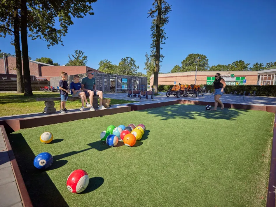 Vader en kinderen kijken toe terwijl een vrouw het biljartvoetbalspel speelt bij Recreatiepark de Leistert.