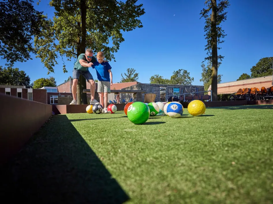 Vader en zoon mikken samen op de kleurrijke ballen tijdens een potje biljartvoetbal op het park in Roggel.
