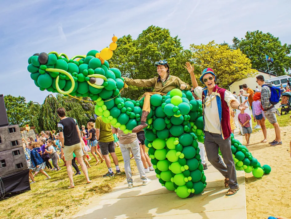 Two entertainers walk across the park with a green balloon dragon during an event at BillyBird Drakenrijk.