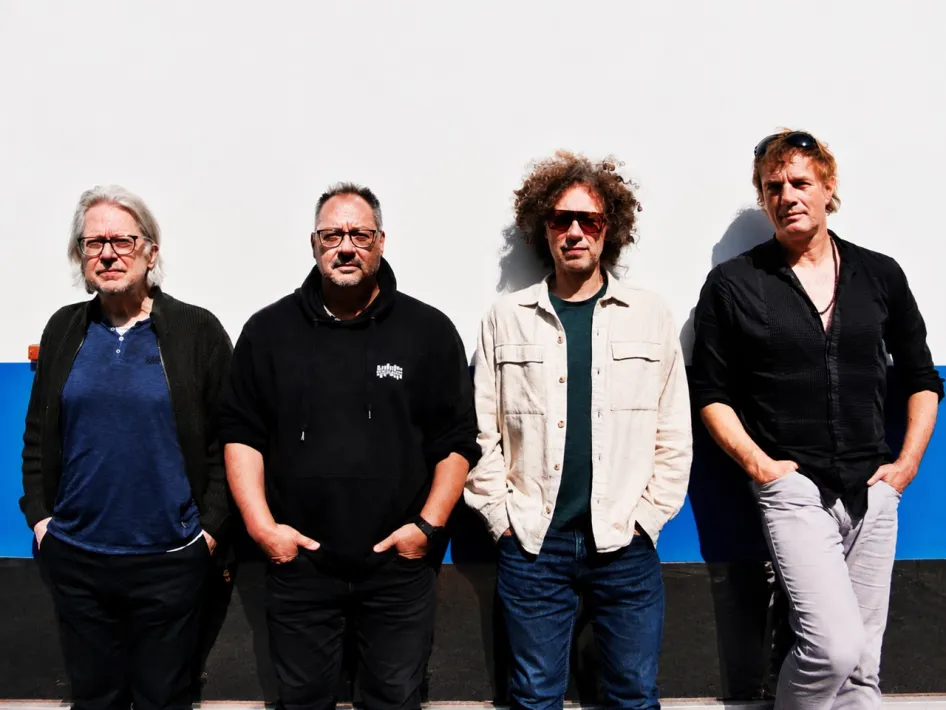 De bandleden van Blowbeat poseren naast elkaar voor een witte muur in de aanloop naar hun concert.