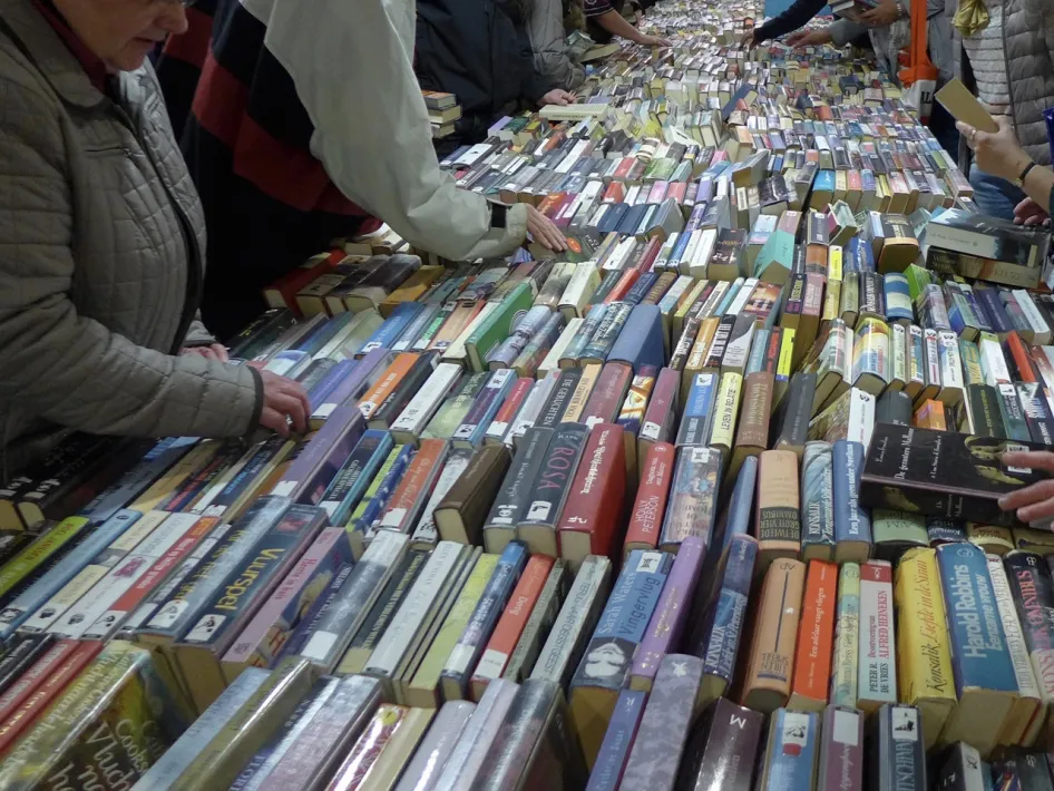 Bezoekers zoeken tussen lange tafels vol boeken tijdens de Boekenbeurs Vincentius Roermond.