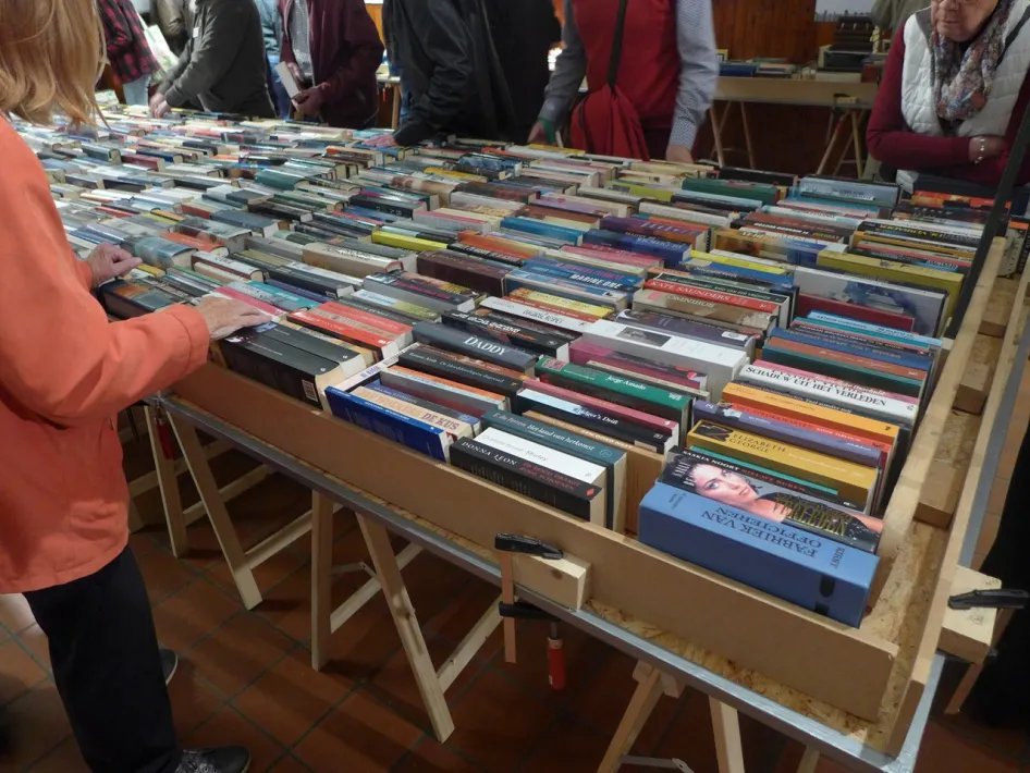 Bezoekers bekijken boeken in houten bakken tijdens de Boekenbeurs Vincentius Roermond.