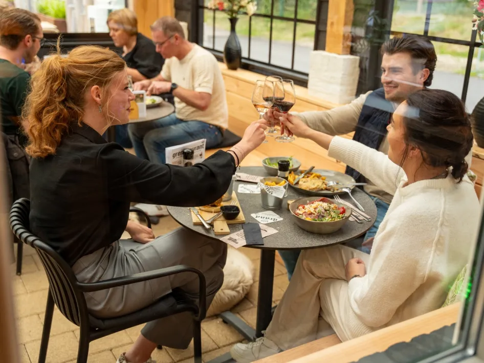 Drei junge Leute stoßen mit einem Glas Wein bei einem gemütlichen Mittagessen im Restaurant an.