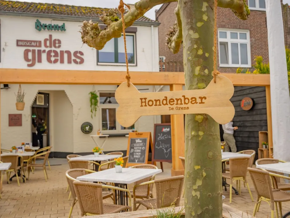 Schild „Dog Bar The Border“ in Form eines Knochens an einem Baum auf der Terrasse des Waldcafés.