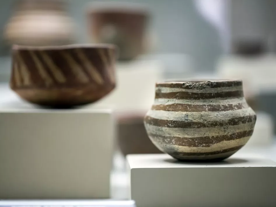 Een verzameling aardewerken potten uit de bronstijd, tentoongesteld op witte sokkels. De eenvoudige patronen en vormen weerspiegelen de stijl en het vakmanschap van deze historische periode.