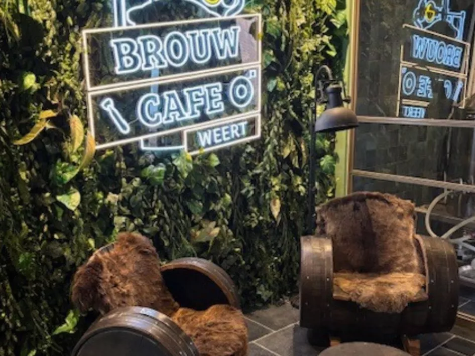 Een knusse zithoek met met bont beklede stoelen, een groene muur en een verlicht neonbord met het logo van Brouwcafé Weert.