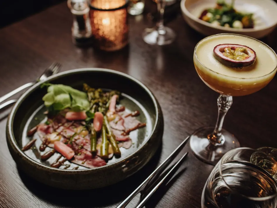 Beautifully prepared appetizer with carpaccio, vegetables and sauce, served alongside a tropical dessert in a cocktail glass.