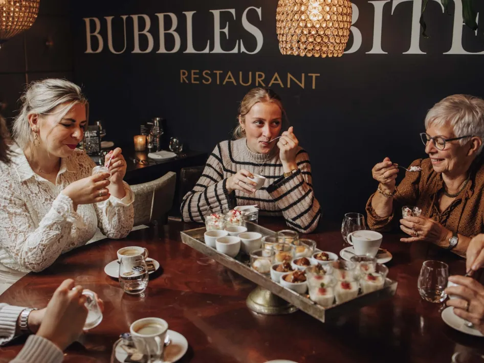 Gemütliche Atmosphäre am Tisch bei Bubbles & Bites, wo die Gäste gemeinsam eine Dessertverkostung und Kaffee genießen.