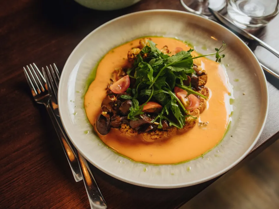Court with grilled cauliflower, sauce and a fresh topping of arugula, beautifully presented on a white plate.