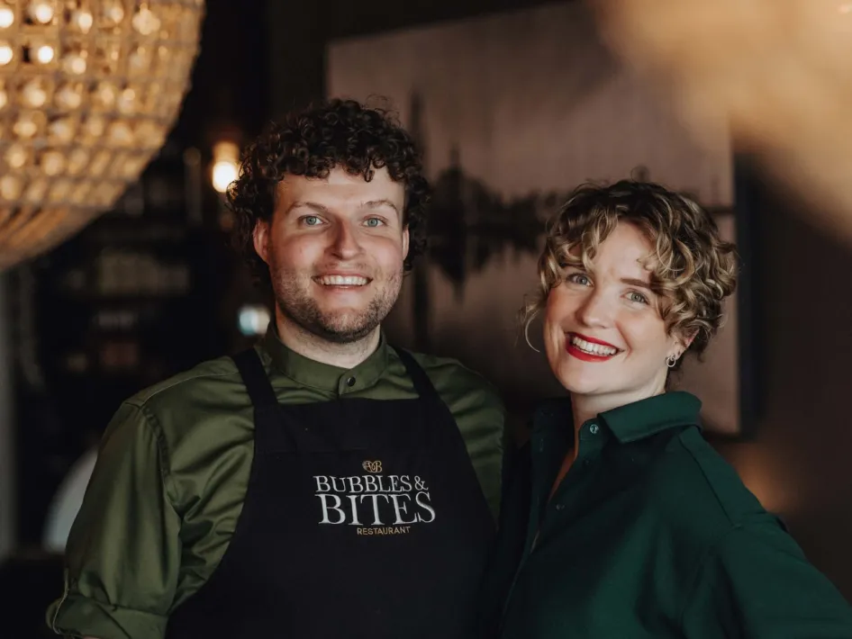 Two beaming employees of Bubbles & Bites restaurant pose together in a warm and stylish setting.