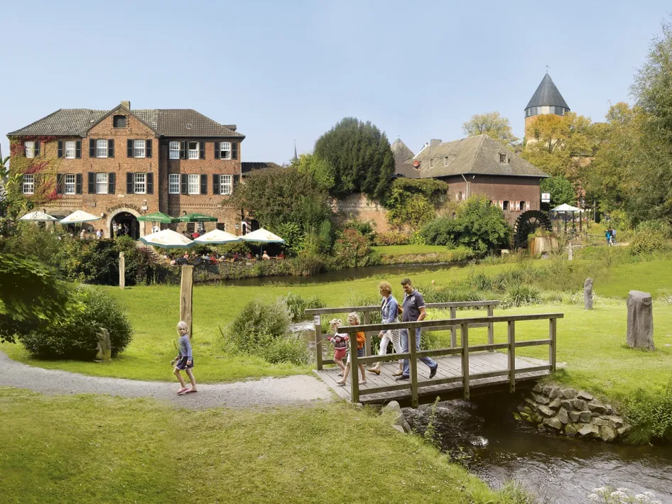 Familienspaziergang im Park von Schloss Brüggen, wo sich die Tourist-Information Brüggen befindet, mit Terrasse und Wassermühle im Hintergrund.