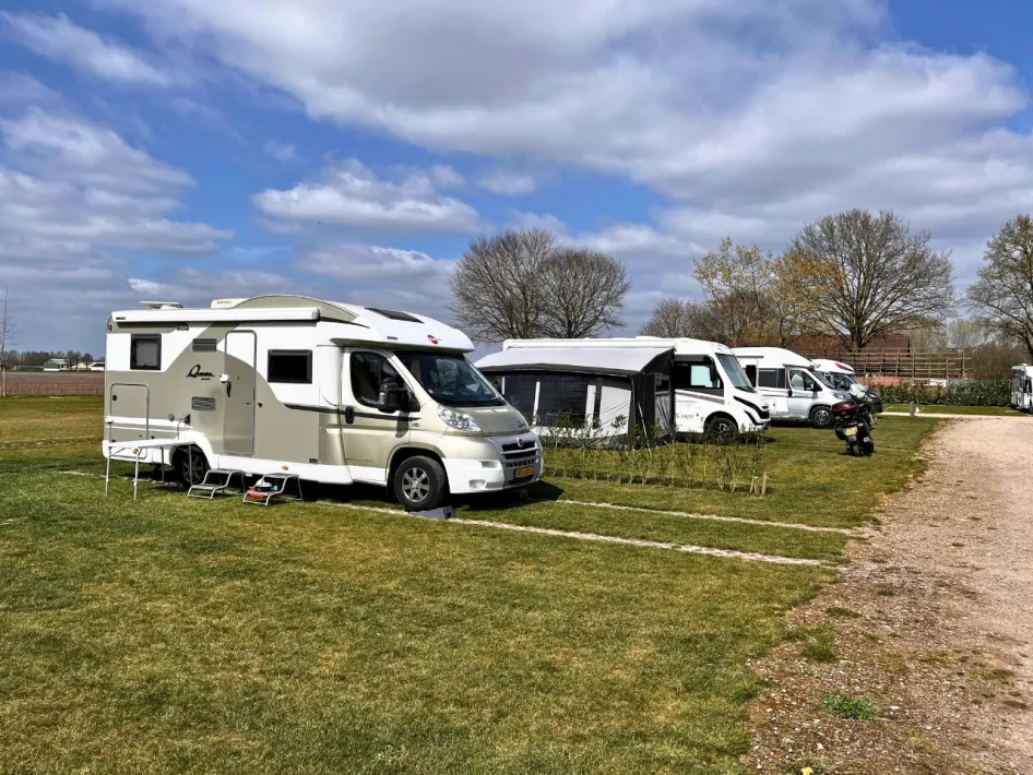 Wide view of a green RV site with several RVs and a dirt road surrounded by trees and a rural setting.